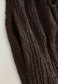 Tissu tricoté marron foncé avec un motif torsadé texturé, présenté en gros plan avec des plis et des ombres douces.