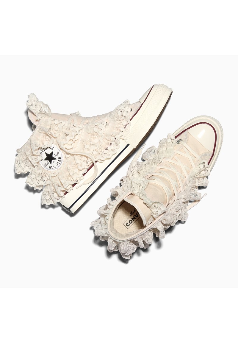 Beige Converse High-Top-Sneaker, verziert mit cremefarbenen Spitzenrüschen an den Seiten, der Zunge und dem Knöchelbereich.