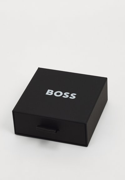 Boîte rectangulaire noire avec une finition mate lisse, présentant un logo "BOSS" en argent sur le dessus et une languette en tissu pour l'ouverture.