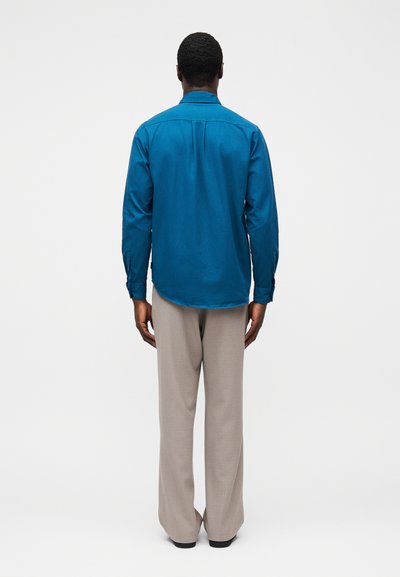 Μπλε πουκάμισο με μακριά μανίκια, μανσέτες με κουμπιά, πίσω ώμος και στρογγυλεμένη άκρη, συνδυασμένο με ανοιχτογκρι παντελόνια με φαρδιά πόδια από λείο ύφασμα.