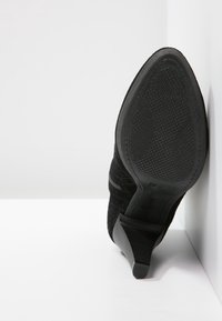 Černá vysoká klasická bota s texturovaným vnějším materiálem, špičatou špičkou a vroubkovanou gumovou podrážkou. Disponuje elegantním designem podpatku.