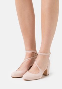 Scarpe con tacco in suede rosa chiaro, con punta arrotondata, cinturino alla caviglia e tacco a blocco. Presentano un design con ritagli per un tocco di originale.
