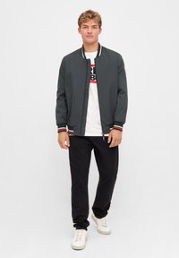 Mörkgrön bomberjacka med vita och röda randiga manschetter, matchad med en vit grafik t-shirt och svarta byxor, bärs med vita sneakers.