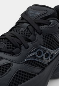 Scarpa da corsa nera con tomaia in mesh, suola in gomma solida, dettagli testurizzati e logo arrotondato sul lato.