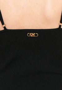 Čierny rebrovaný top s tenkými ramienkami a zlatým logom na chrbte. Hladká textúra s jemným leskom.