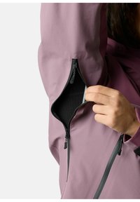 Veste waterproof violette avec une poche zippée sur la manche, doublure intérieure noire et fermeture éclair noire contrastante.