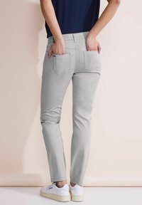 Jasnoszare dżinsy o slim-fit z tylnymi kieszeniami, w połączeniu z białymi sneakersami. Materiał wydaje się miękki o gładkiej strukturze.