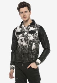 Schwarz-weiße Jacke mit einem grafischen Druck von Landschaften, Nietenkragen und kontrastierenden Lederärmeln. Knopfleiste und zwei Brusttaschen.