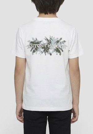 Bambino che indossa una maglietta bianca con silhouette nere di palme e la scritta "ANTONY MORATO" sulla schiena, abbinata a pantaloni neri.