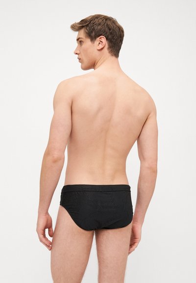 Maillots de bain noirs avec un motif texturé, présentant un design épuré et une taille élastique, vus de dos sur un fond neutre.