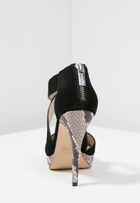 Zwarte suède high-heeled schoen met een geprinte slangenhuid hak. Voorzien van een ritsluiting en een uitsnijding, die een beige inlegzool onthult.