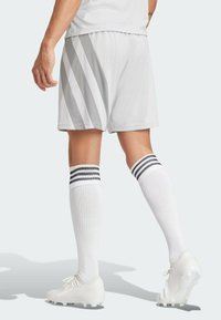 Vita atletiska shorts med grå randningar, kombinerade med vita knästrumpor med svarta ränder. Bärs med vita fotbollsskor.