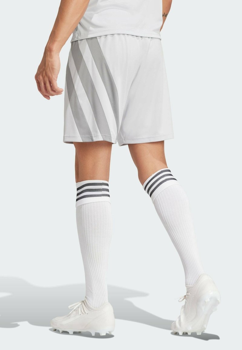 Vita atletiska shorts med grå randningar, kombinerade med vita knästrumpor med svarta ränder. Bärs med vita fotbollsskor.