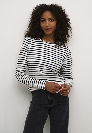 Langärmliges schwarz-weiß gestreiftes Hemd mit einem blauen Herzdetails auf der Brust, kombiniert mit hochgeschnittenen dunklen Jeans.