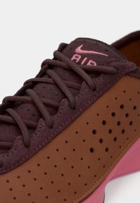 Κοντινό πλάνο μπορντό και καφέ αθλητικού παπουτσιού Nike Air με διάτρητο πλαϊνό μέρος, μπορντό κορδόνια και ροζ τμήμα σόλας.