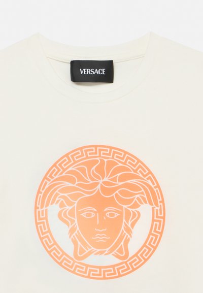 Κρεμ μπλουζάκι με μαύρη ετικέτα Versace και πορτοκαλί λογότυπο κεφαλής Μέδουσας περιτριγυρισμένο από ελληνικό κλειδί στο στήθος.