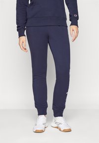 Pantalons de jogging en molleton bleu marine avec taille élastique, poignets côtelés et logo brodé sur la jambe gauche. Texture lisse sur l'ensemble.