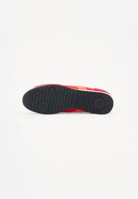 Red sneaker with a rubber black sole, textured for grip, featuring orange and white accents on the side and a smooth upper material.