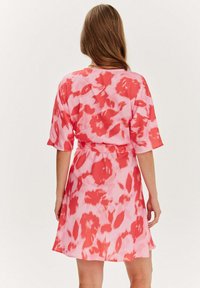 Krátké růžové šaty s červeným květinovým vzorem, volný střih a krátké rukávy. Šaty jsou v pase stažené odpovídajícím páskem.