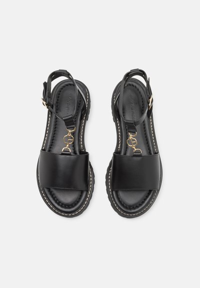 Černé kožené sandály na otevřenou špičku s pásky kolem kotníků, zlatými přezkami, polstrovanou stélkou a bílým prošitím na silných gumových podrážkách.