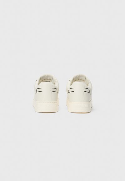 Sneakers blancs avec une finition en cuir lisse, bout rond, col rembourré moelleux et lignes noires subtiles sur le talon.