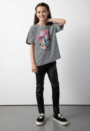 Pasiasty czarno-biały t-shirt z kwiatowym wzorem, zestawiony z błyszczącymi czarnymi legginsami i czarnymi trampkami z białą podeszwą.