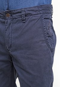 Chinos de mezcla de algodón azul marino con una textura suave, con cierre de botón y bolsillos laterales. El diseño incluye detalles de costura sutiles.