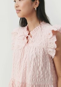Rosa texturerad blus med volangärmar och en nyckelhålsknytning vid halsringningen, i ett mjukt, skrynkligt material och lagerdesign.
