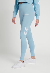 Ljust blå leggings med vitt Hummel-logotyp och chevronmönster på sidorna, tillverkade av stretchigt tyg för komfort och rörlighet.