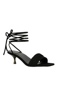 Schwarze Wildleder-Absatzsandalen mit zwei breiten Riemen, einem schmal zulaufenden Absatz und kreuzenden Knöchelbindern mit einer Schleifendetail. Glatte Sohle im Inneren.