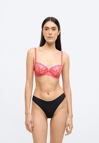 Ροζ δαντελένιο σουτιέν με μπανέλα και λουλουδάτο σχέδιο, ρυθμιζόμενους ιμάντες και φιόγκο στο κέντρο· συνοδεύεται από μαύρο κάτω μέρος εσώρουχου με χαμηλή μέση.