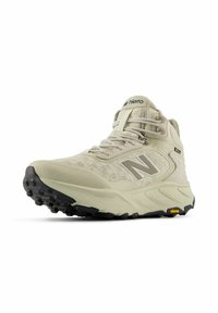 Zapatilla de senderismo de un beige claro con parte superior de malla, acentos grises y suela de goma negra. Presenta un collar acolchado y suela de tracción Vibram.