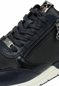 Sneaker in pelle nera e tessuto con chiusura a zip, superficie testurizzata e lacci intrecciati. Dettagli includono accessori metallici e suola bianca.