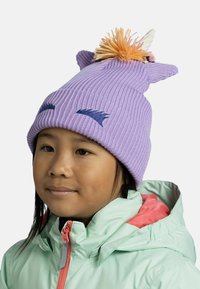 Gorro de punto acanalado morado con dos orejas puntiagudas, pompón decorativo de varios colores y acentos bordados en azul marino. Lleva puesto una chaqueta verde menta.