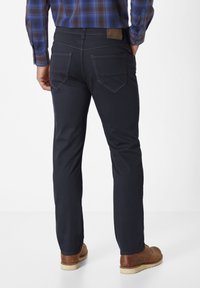 Navy blue trousers in cotton blend with a slim fit, featuring two back pockets, contrasted stitching, and a leather brand patch on the waistband.