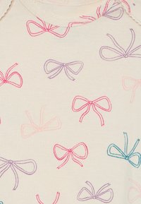 Bomullstoff med en kremfarget bakgrunn og broderte bue mønstre i rosa, lilla og blått. Myk tekstur, rund hals og korte ermer.