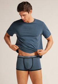 Camiseta azul de manga corta, combinada con bóxers azul oscuro que presentan una banda elástica negra en contraste y detalles de costura.