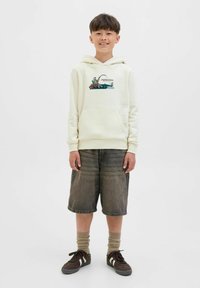 Haut à capuche crème avec un graphique de pêche, poche avant, associé à un short en denim gris et des baskets marron. Manches à nervures et chaussettes remarquables.