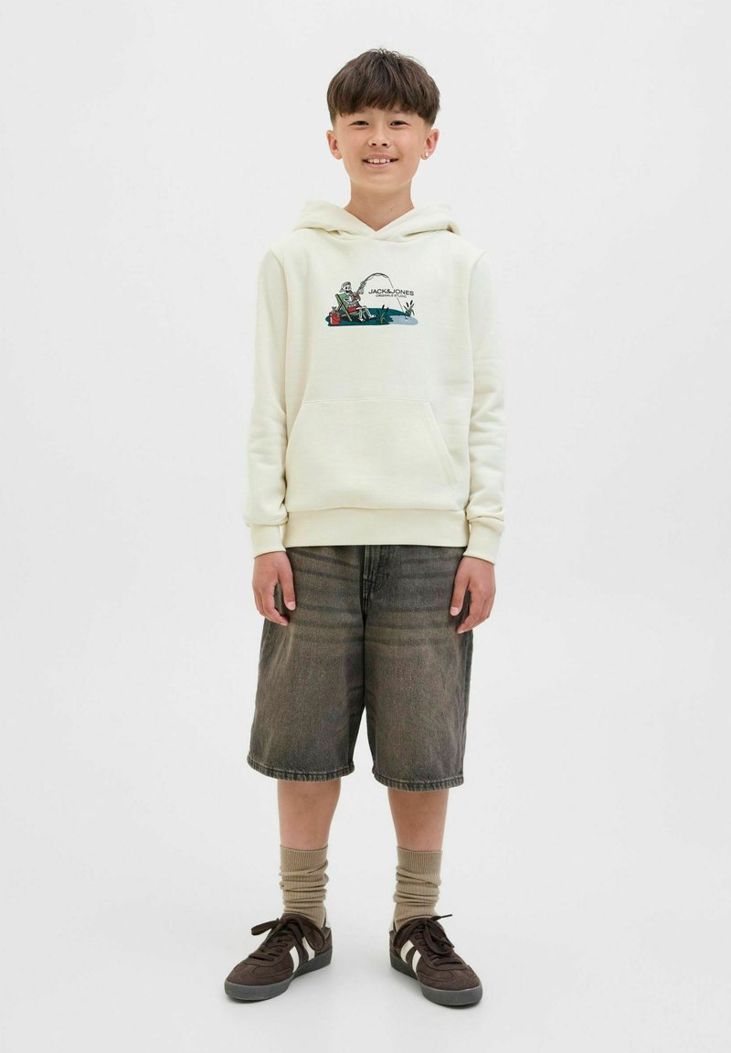 Haut à capuche crème avec un graphique de pêche, poche avant, associé à un short en denim gris et des baskets marron. Manches à nervures et chaussettes remarquables.