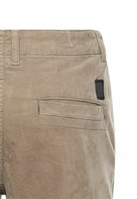Beige corduroy bukser med en baglomme med en diskret sort label, struktureret overflade og standart taljebånddesign.