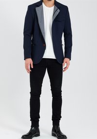 Mörkblå blazer med slag, grårandig foder, två framfickor, knappstängning, kombinerad med figurnära svarta byxor och glänsande svarta stövlar.