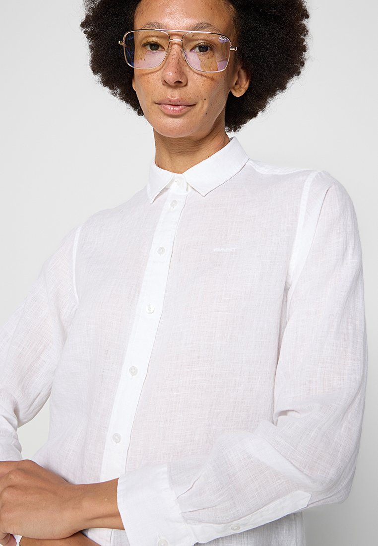 Biała lniana koszula z guzikami, z klasycznym kołnierzykiem, wykonana z fakturowanej tkaniny, z długimi rękawami i mankietami na guziki. Dyskretne logo na klatce piersiowej.