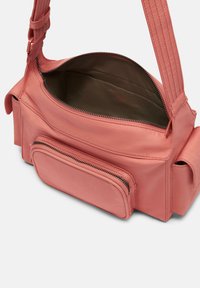 Różowa skórzana torba na ramię z główną komorą na zamek, wewnętrznymi kieszonkami oraz małą przednią kieszonką na zamek. Zawiera teksturowany pasek.