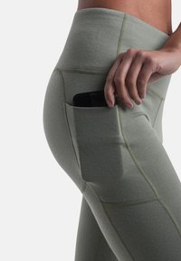 Olivenfarvede leggings med en glat tekstur, der har en sidelomme til opbevaring af en smartphone og kontrasterende søm-detaljer.