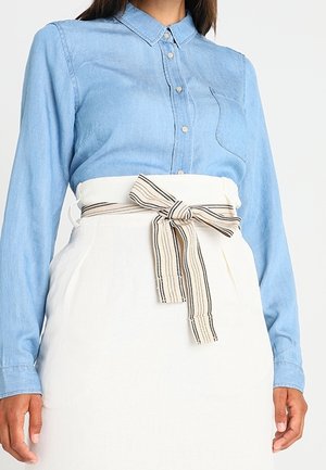 Lyseblå denimskjorte med krave og enkelt brystlomme, kombineret med et hvidt skørt med et stribet stofbælte i taljen.