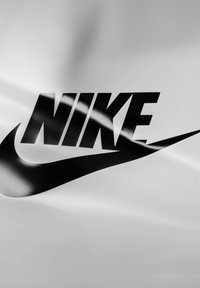 Svart Nike-logo med en swoosh-design trykt på en glatt, hvit bakgrunn. Logoen har fete, store bokstaver.