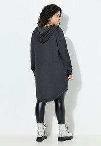 Felpa nera lunga con orlo curvo, realizzata in tessuto morbido. Abbinata a leggings neri lucidi e stivaletti alla caviglia argentati con lacci.