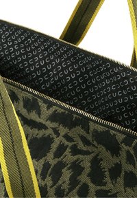 Gros plan d'un sac en tissu imprimé léopard vert et noir ouvert, avec des anses rayées jaunes et noires et une fermeture éclair dorée visible.