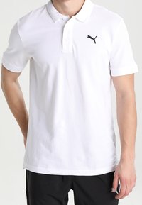 Bílá polo košile vyrobená z bavlny, s límcem na tři knoflíky, krátkými rukávy a černým logem Puma na levé části hrudi.