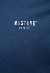 Tengerészkék pamut póló kerek nyakkal. Az elején fehér színű szöveggel ellátott "MUSTANG" és "SINCE 1932" felirat található. Simább tapintású.